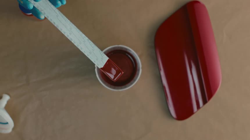 A person mixes red paint with a ruler