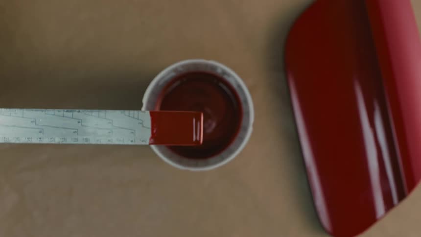 A close up of a man wearing gloves mixing red paint in a workshop