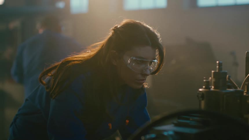 A woman working with a lathe inside a dimly lit workshop