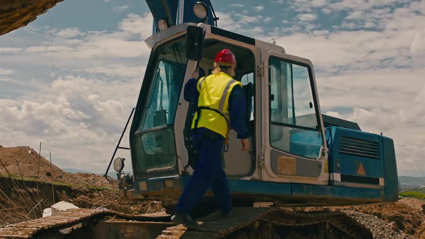 Worker with helmet entering inside an excavator at a construction site