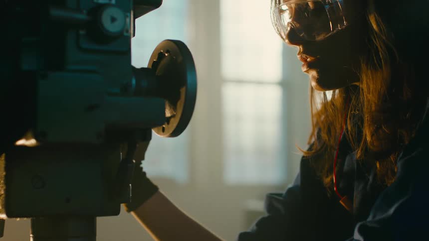 A woman is operating a drill press in a dimly lit workshop