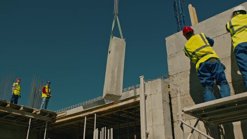 Construction workers in high visibility jackets installing a large concrete column on a building site