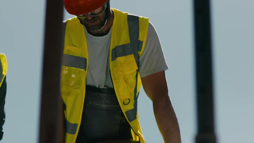 Two men in protective clothing using a jackhammer drilling concrete into the ground