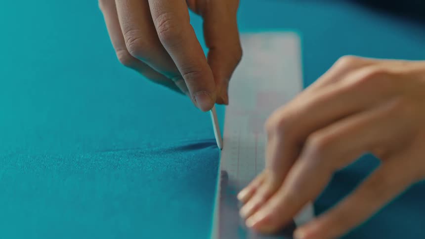 A hand tracing a line over blue cloth using chalk and a ruler
