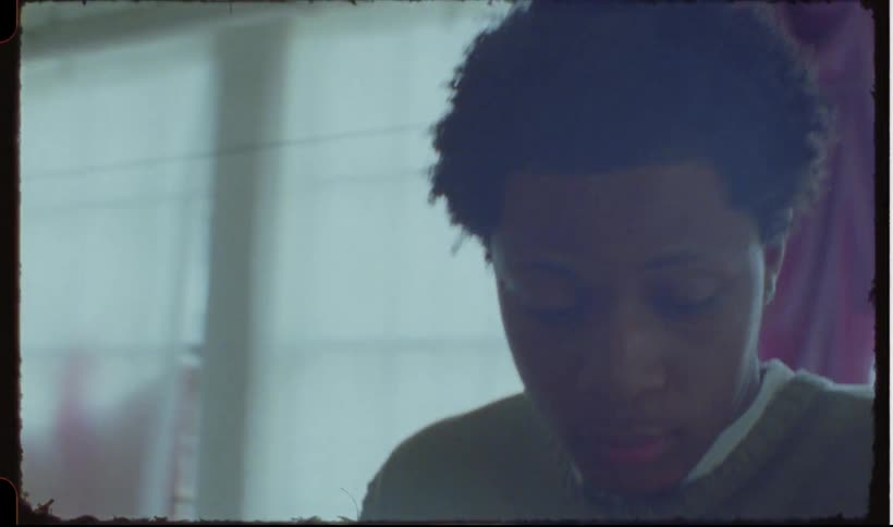 A man with curly hair near large windows caught on vintage film