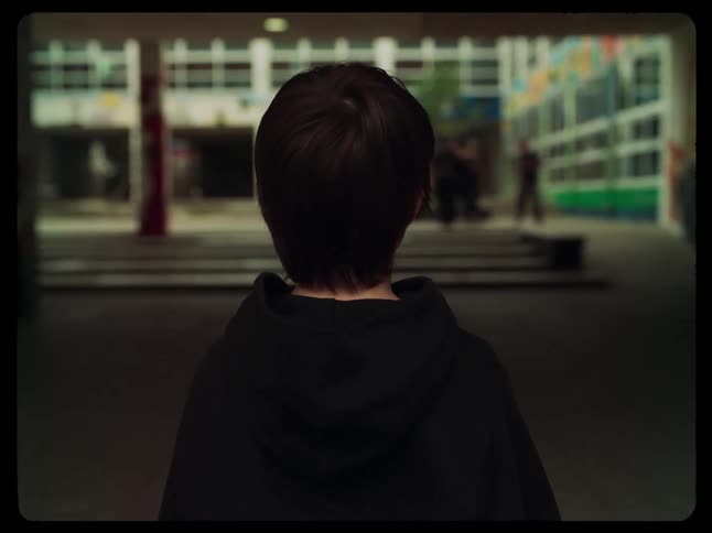 Little boy with his back watching people skateboarding near a small stairs