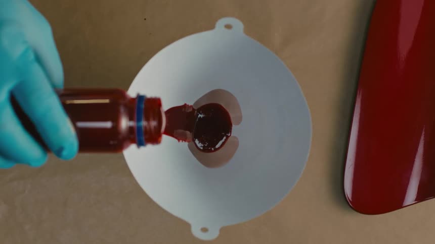 Hand with disposable glove pouring red paint into a white funnel