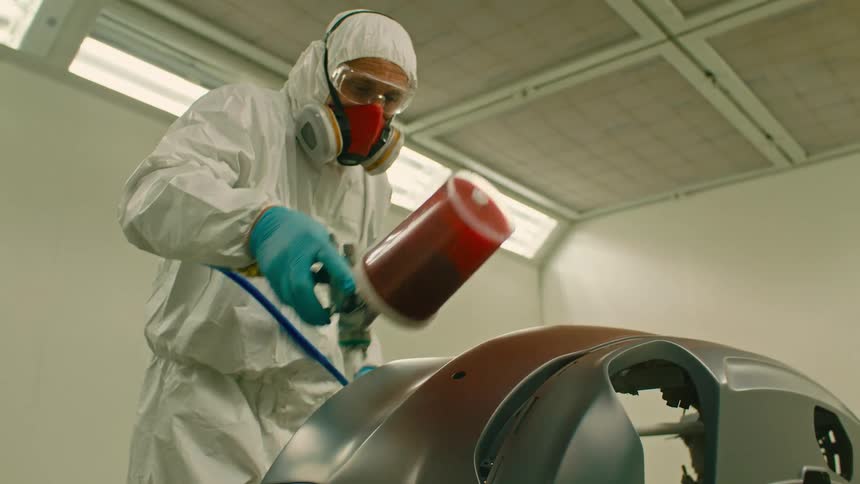 Man with mask and protective glasses painting a part of the car with red paint