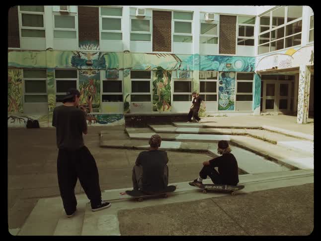 A group of friends look at another skateboarding inside a building with murals