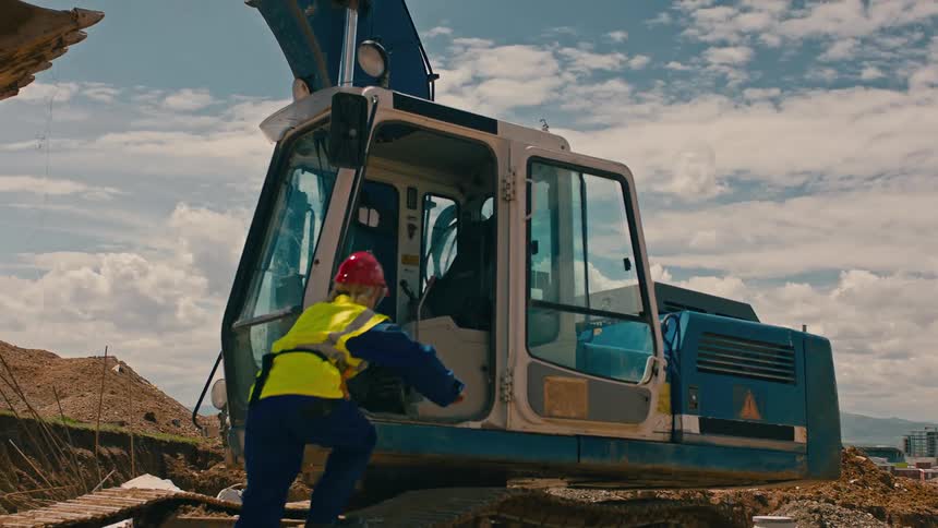 The operator wearing protective equipment gets into the bulldozer prepared for construction tasks