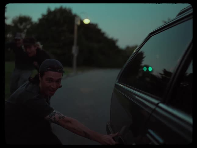 Skateboarding friends hang onto car driving along highway at night