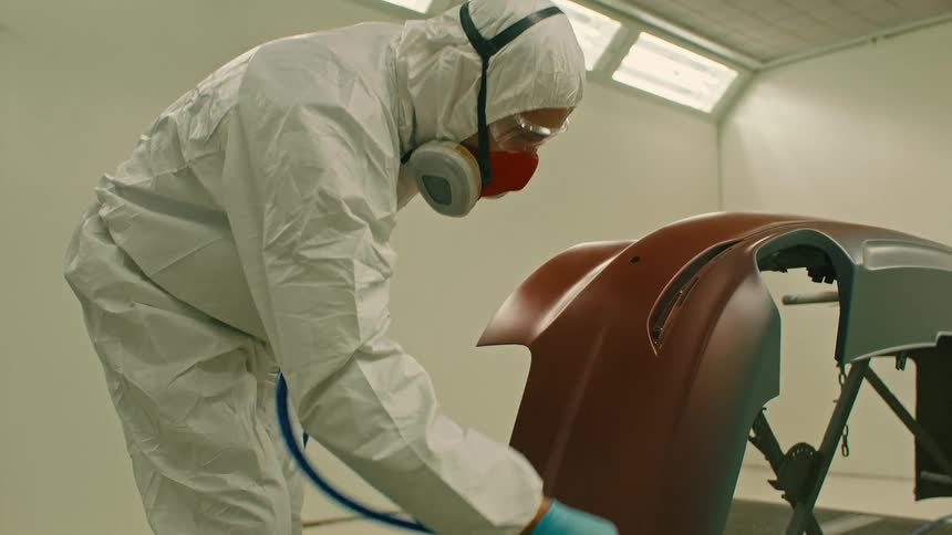 A worker paints a piece of a car in a room