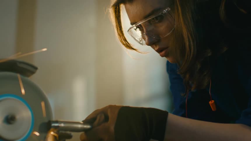Wman scraping a metallic cylindrical object using the machine with spark