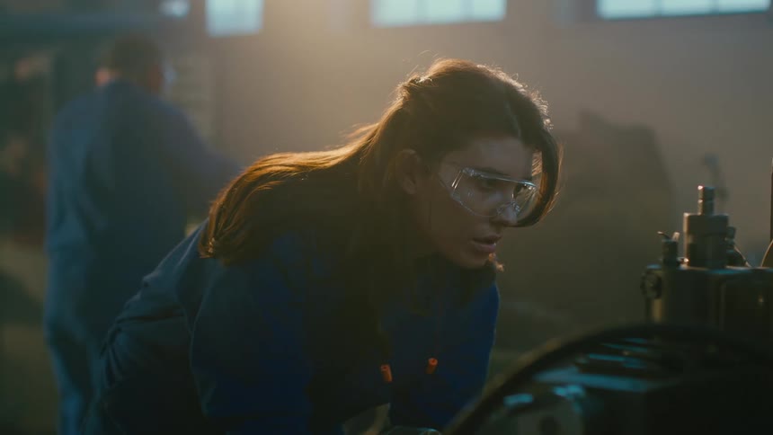 A woman working a lathe in a dimly it workshop