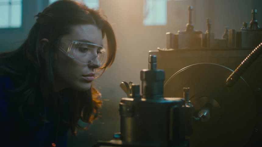A woman adjusting a lathe inside a dimly lit workshop