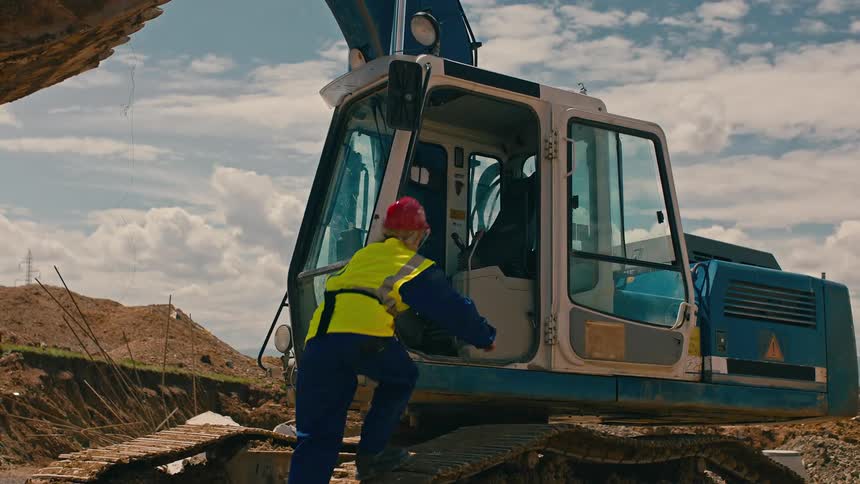 Woman with protective helmet and vest entering a crane at a construction site