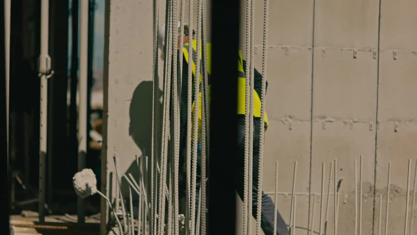 A worker in a yellow vest and a white hardhat is working on a building construction site