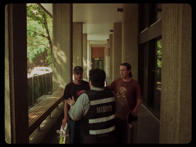 A security guard talking to teenagers with skateboards in a building