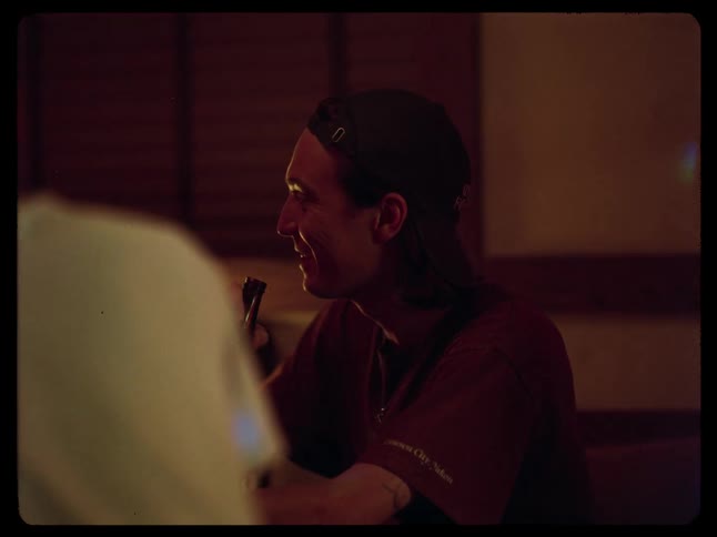 Side view of a man drinking beer seated inside a room with low light
