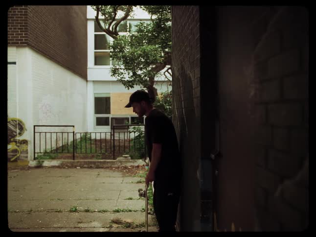 Man skateboarding in an alley and resting on the wall