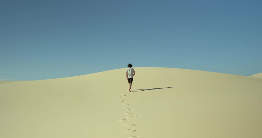 A man is walking up a hill in the desert