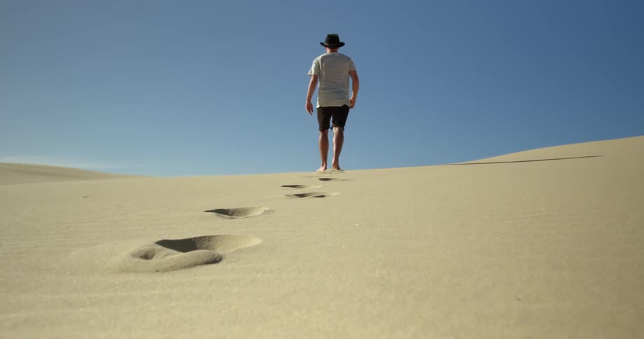 A man in shorts walks across soft sand