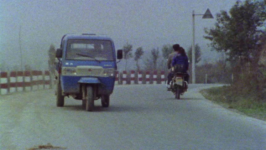 Small truck and a motorbike passing on a curve of a paved road