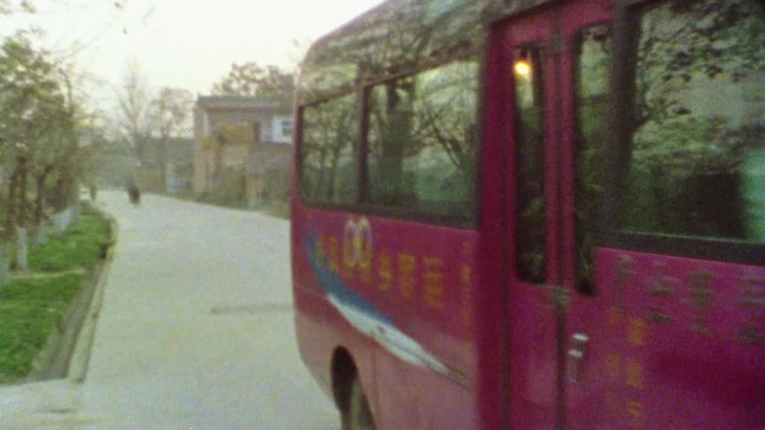 A small bus drives down a road in a suburb