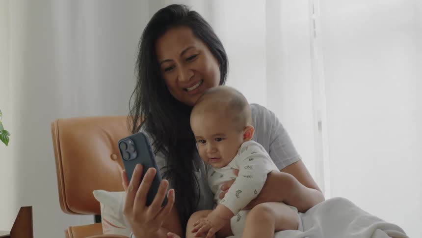 Mother sitting with her baby on her lap and holding an iphone smiling