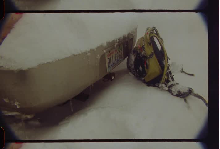 The car and backpack are covered with snow