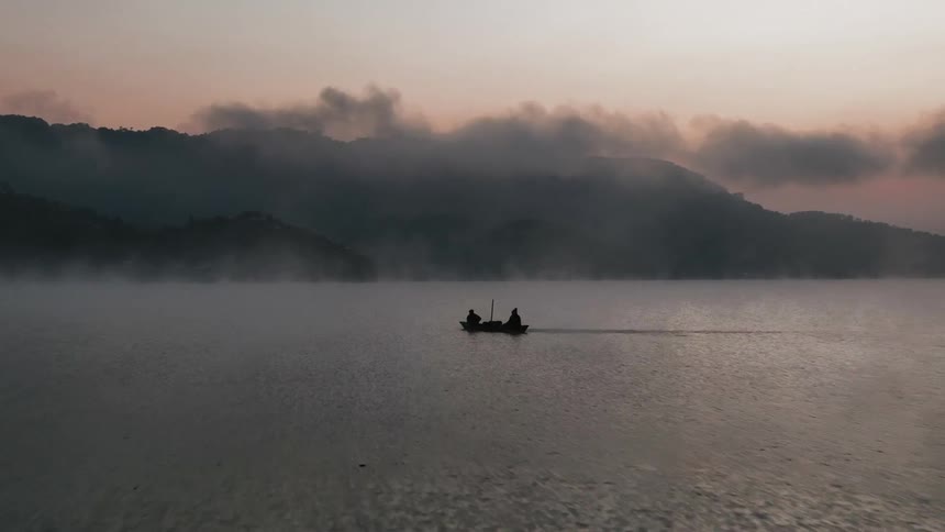 Two people ride in a boat moving through the water with the red sky and coast in the background