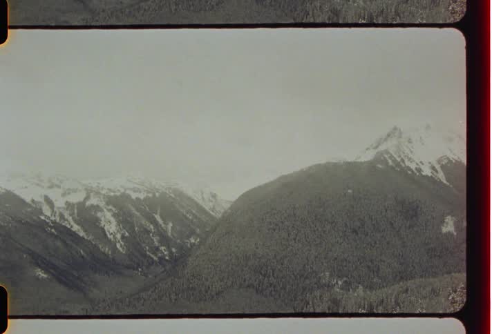 Panorama of mountains with trees and peaks with snow on a cloudy day
