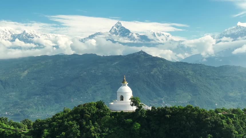 Domed building stands atop forested mountain across water from town at foot of another mountain