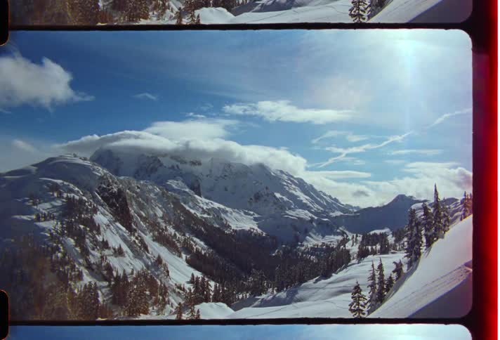 Scattered groves of conifers stand on snowy mountain slopes and the valley between them
