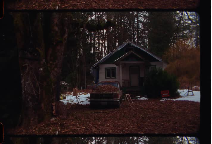 A rustic cabin surrounded by trees with a light dusting of snow on the ground