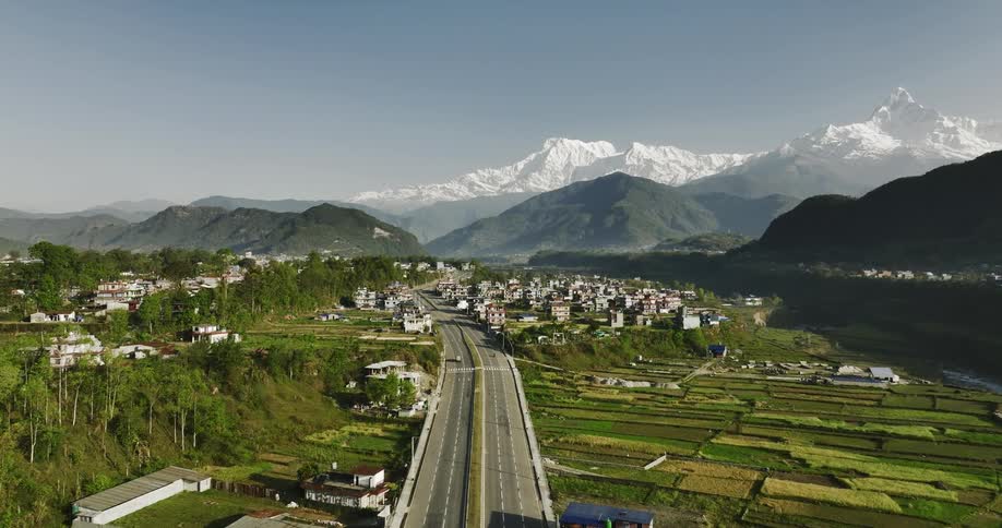 Aerial panorama of a paved road with farm fields and houses around and snowy mountains on the horizon