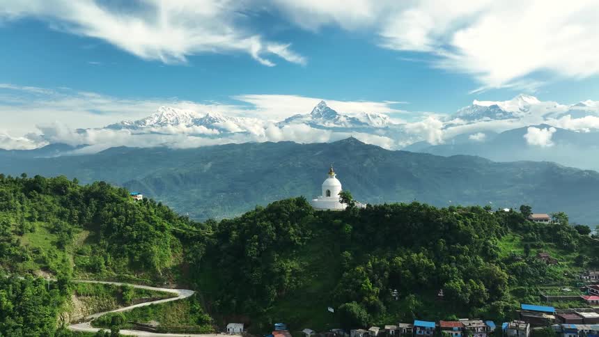 Aerial panorama of a village built by forested mountains and a temple at the top