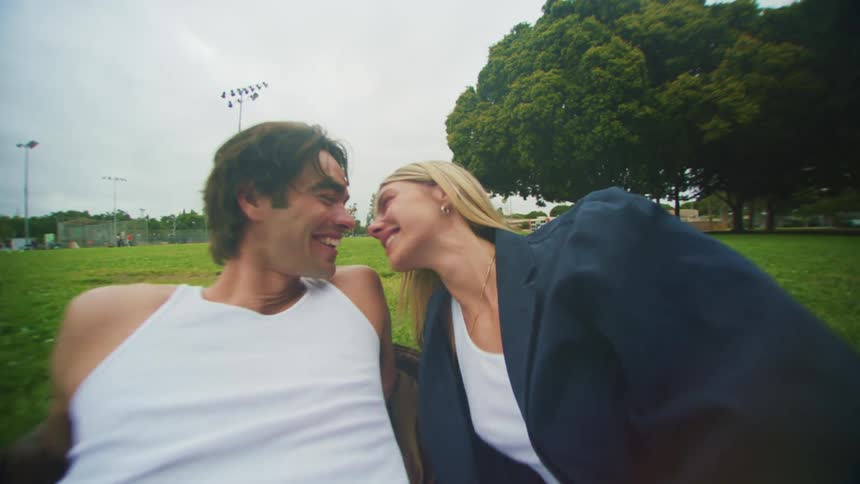 A man and woman kiss while lying on grass in a park