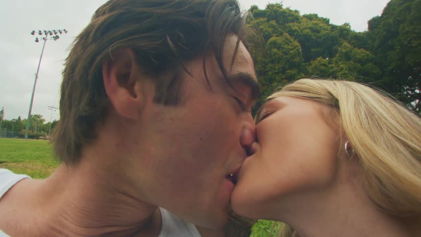 A man and a woman kiss in a park