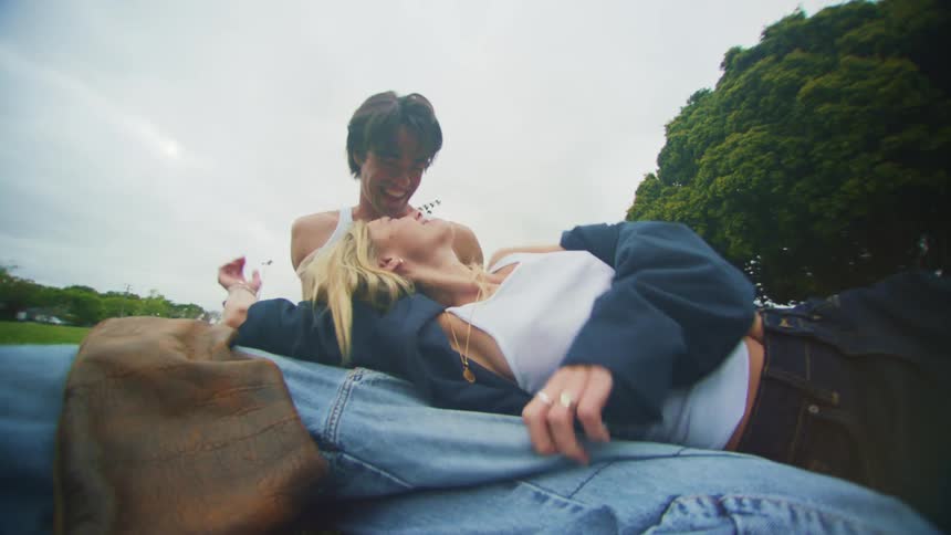 Couple of a man and a woman sitting on the grass in a park kissing romantically