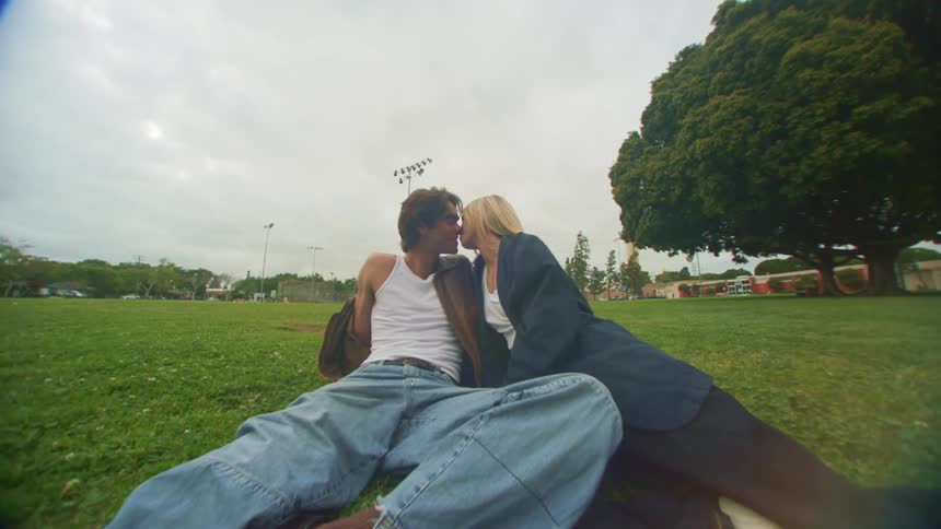 A young couple kissing over the green grass on a park