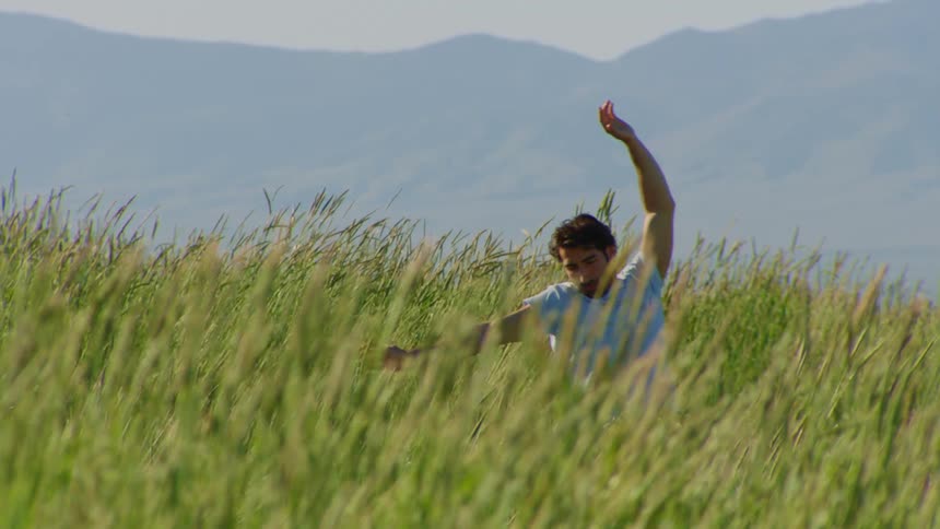 Man dances in field of tall grass while fog obscures the mountain in the background