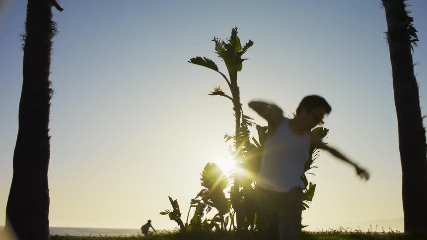 Man dancing next to trees and in the background the silhouette of people riding bicycles on the beach