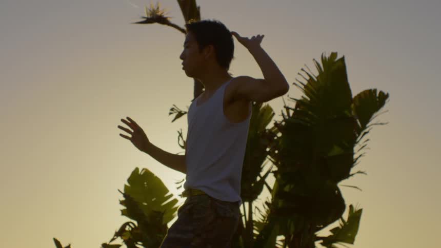 An asian man performs dance moves in front of a tree
