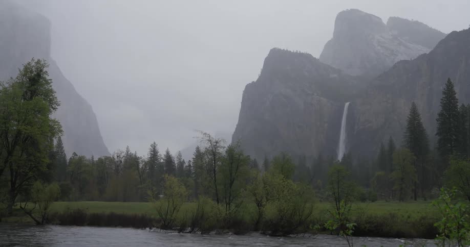 A field with a river and a waterfall coming from a mountain behind it