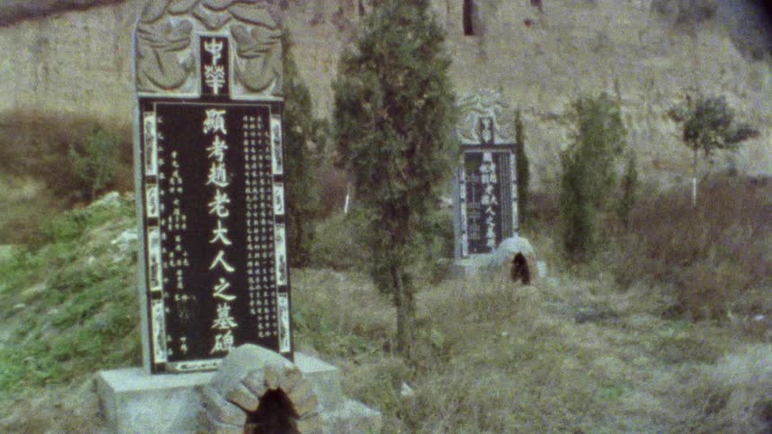 Stone sculptures with letters in asian language in a field with bushes around and in the background a motorcycle passing by