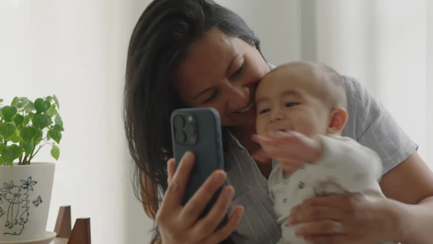 Mother holding a smartphone in front of her baby