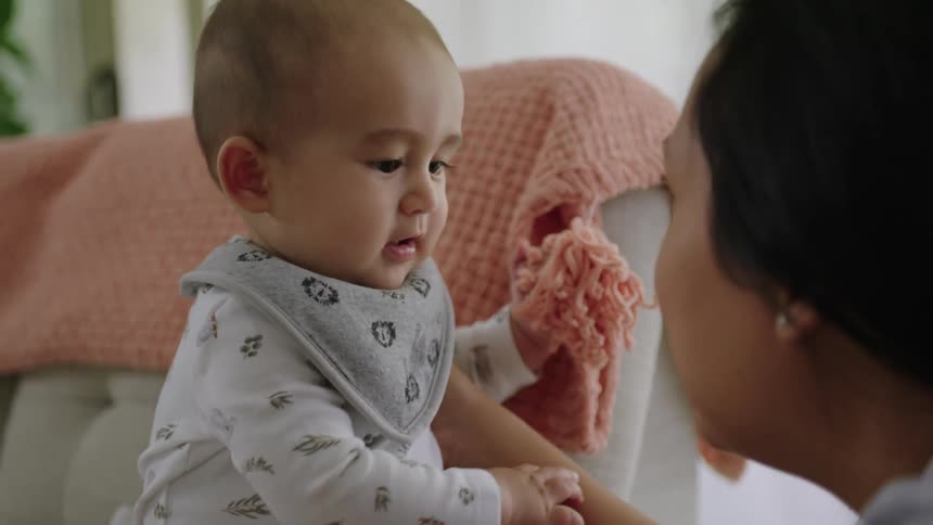 A mother holds and talks to her baby while sitting on the beige couch in the living room