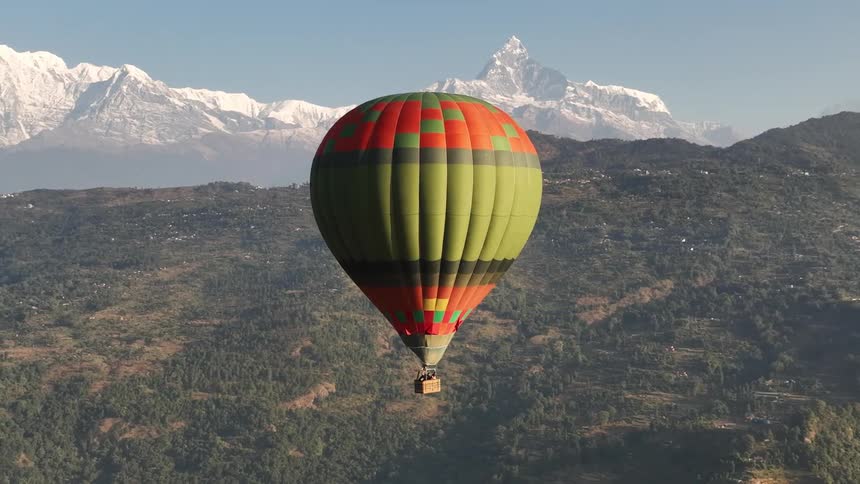 A hot air balloon drifts in the sky with a mountain landscape in the background