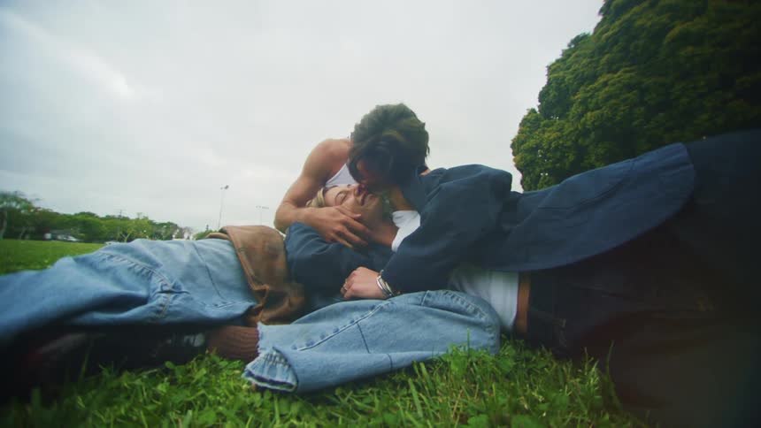 Woman and man in a field kiss while she lies with her head in his lap